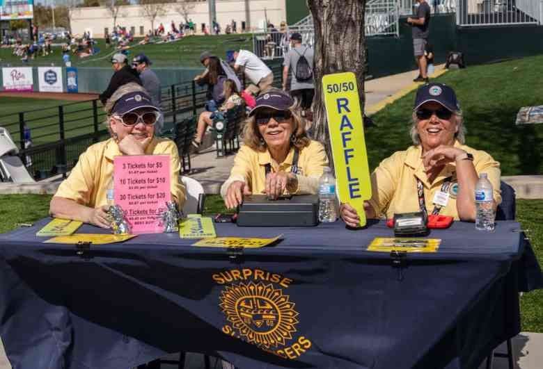 Three people sitting at a table with raffle signs.