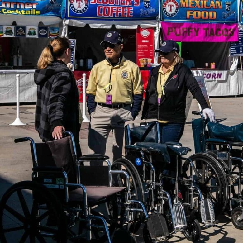 Three people standing next to a row of parked wheelchairs.