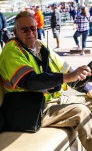 A man in yellow vest sitting on chair next to other people.