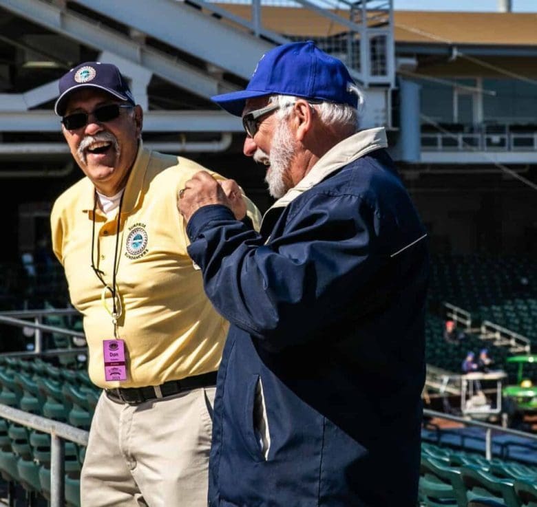 Two men laughing in a stadium with bleachers.