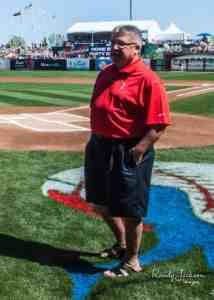 A man in red shirt and black shorts standing on field.