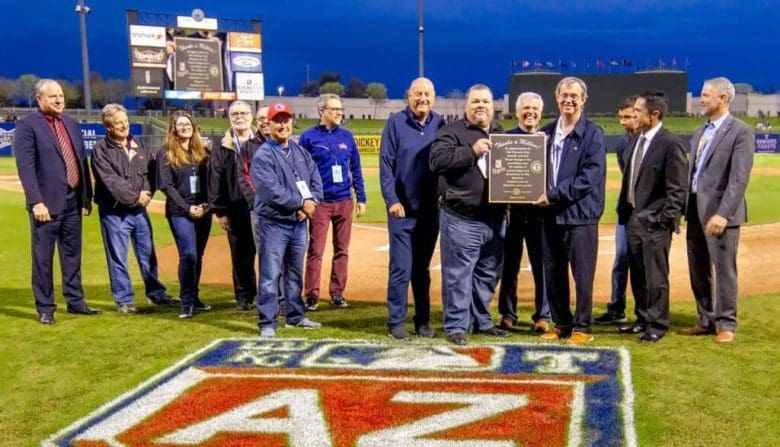 A group of people standing around a baseball field.