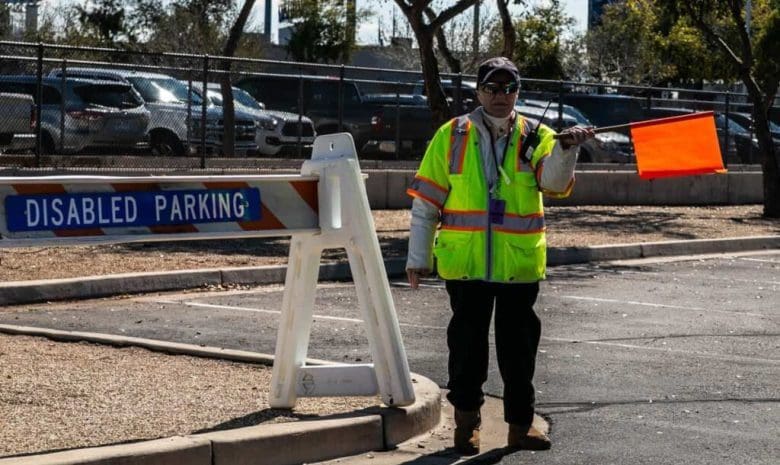 A man in yellow vest standing next to a white sign.