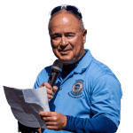 A man in blue shirt holding papers and microphone.